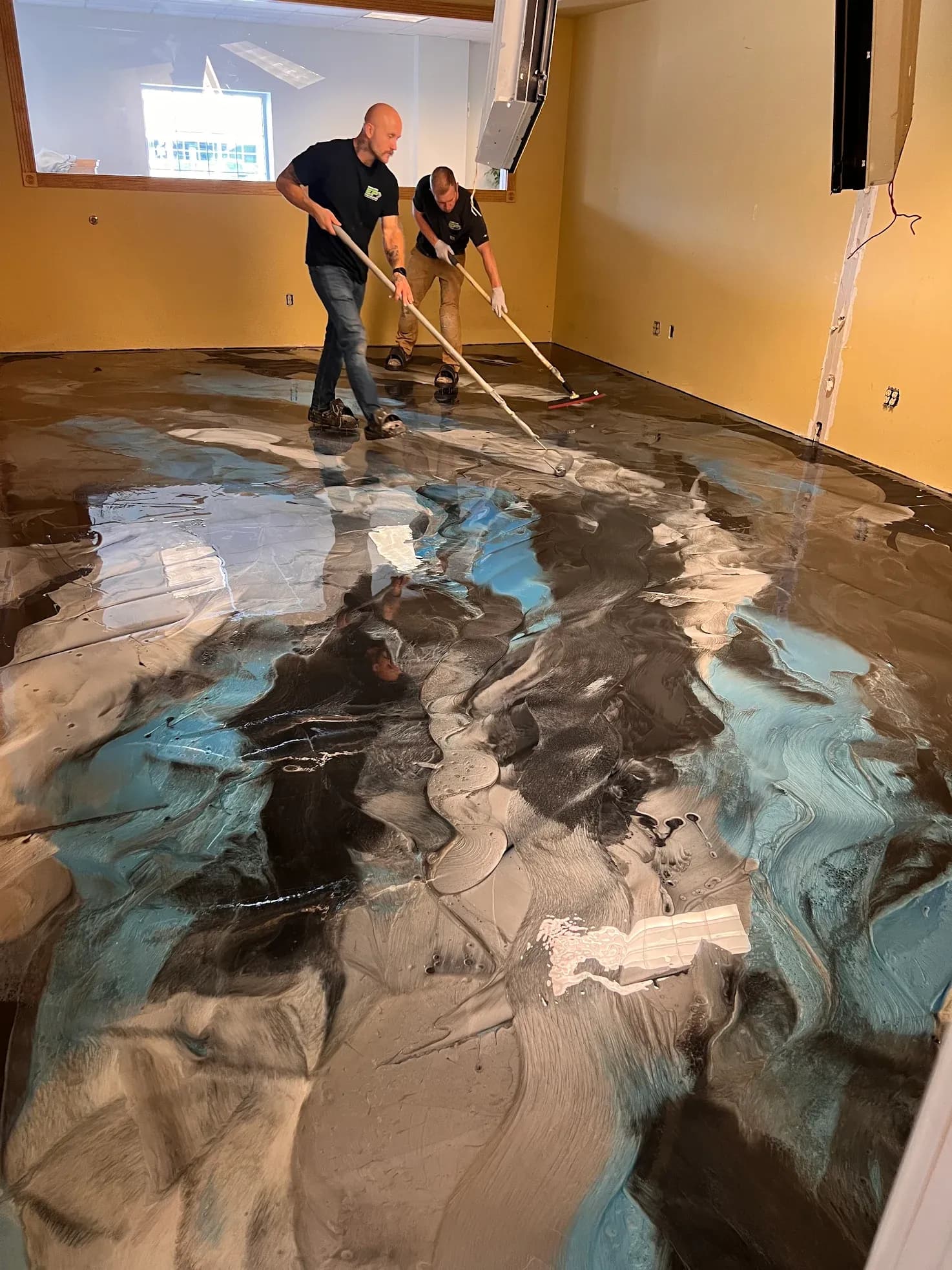 Workers apply a black, blue, and gray concrete coating flooring to an office conference room.