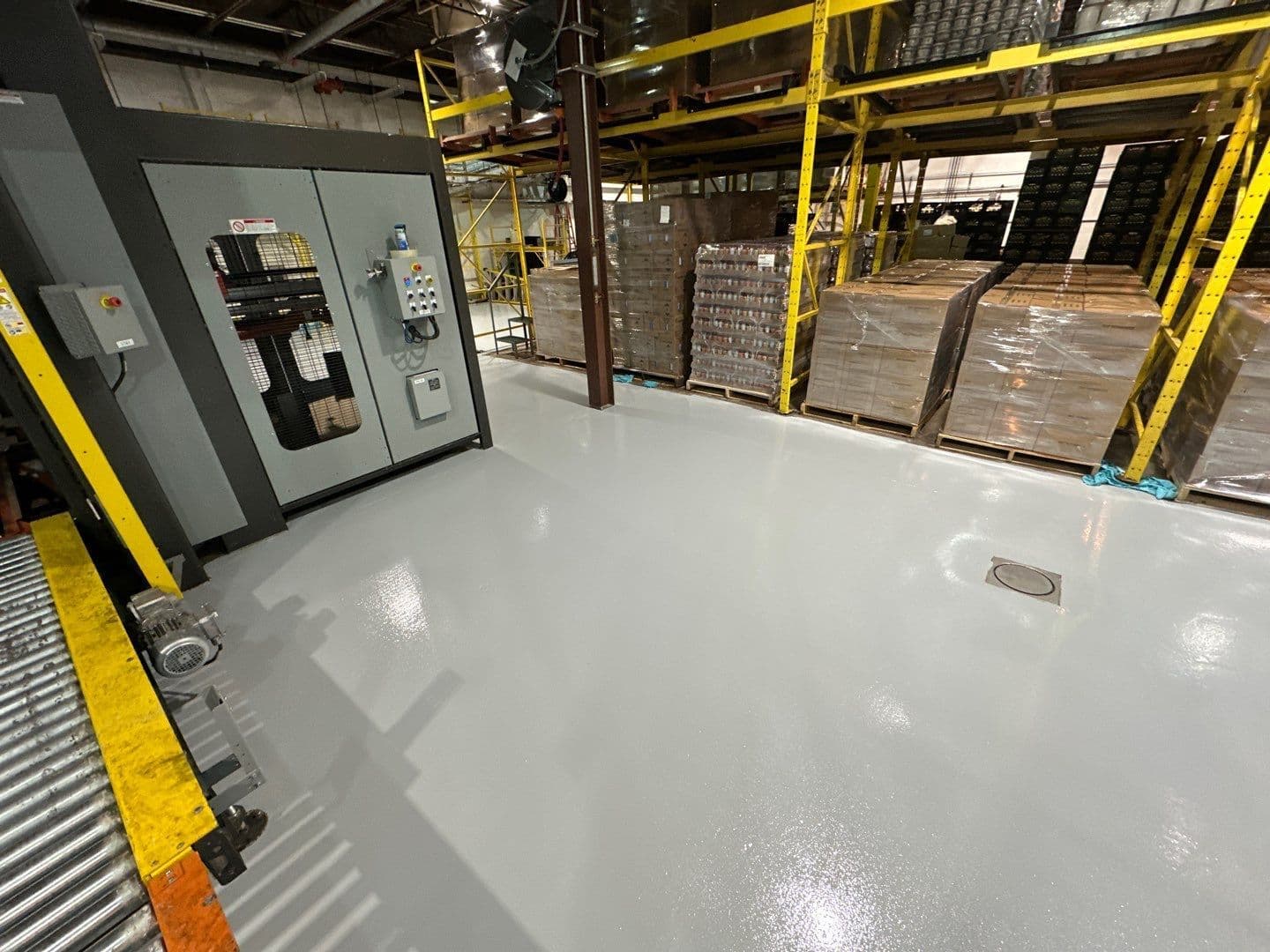 A commercial warehouse space with solid, light gray Urethane cement concrete coated flooring. Pallets are visible in the background.