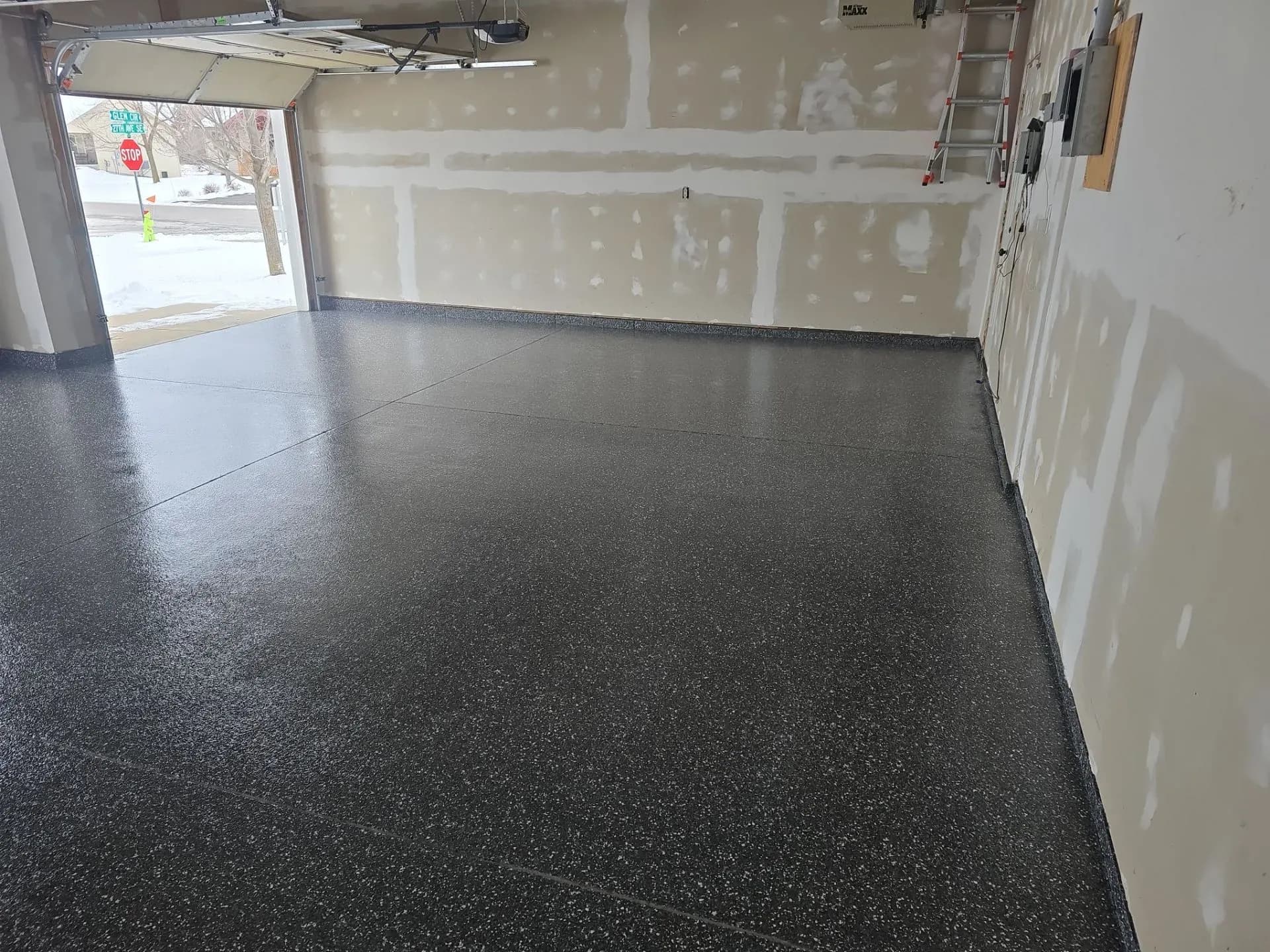 A garage with newly-coated black concrete flooring with light flecks.