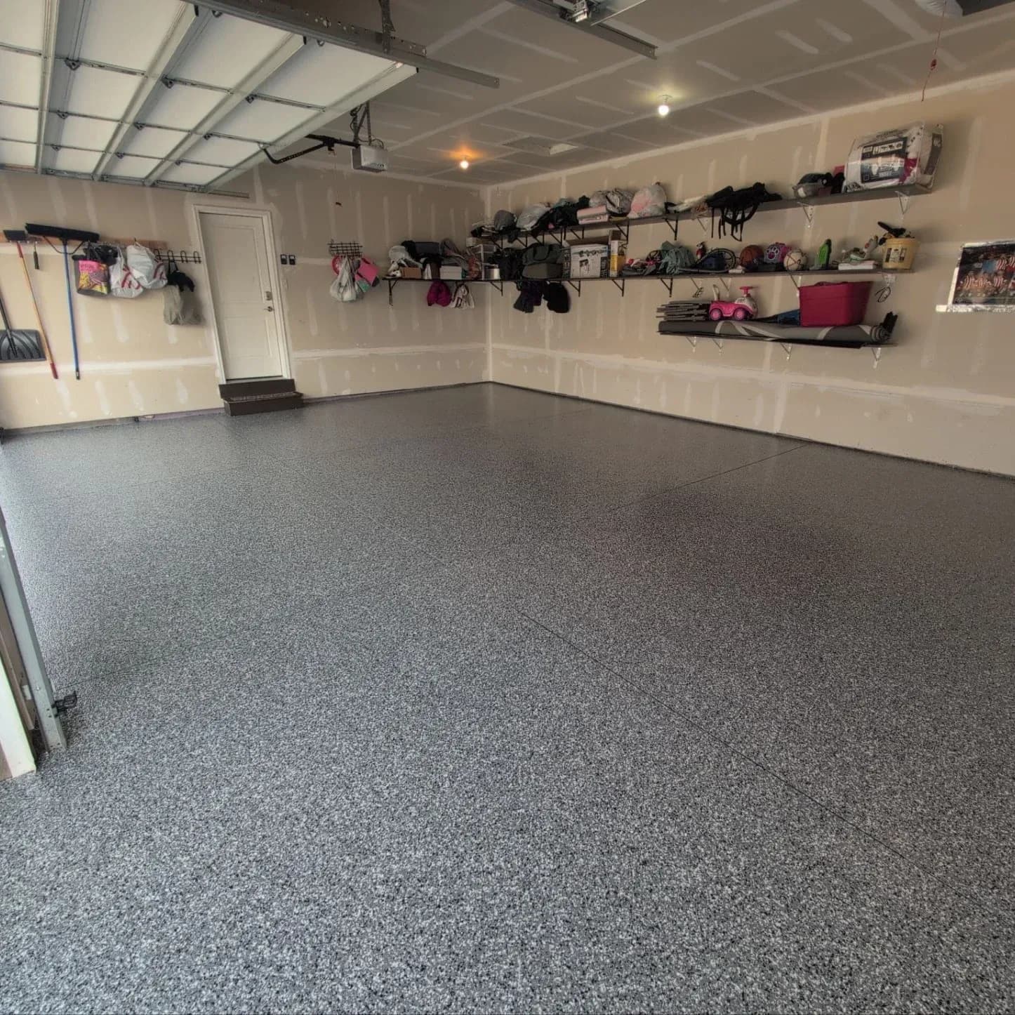 A garage with storage shelving and new gray, black, and white concrete coated Polyaspartic flooring.