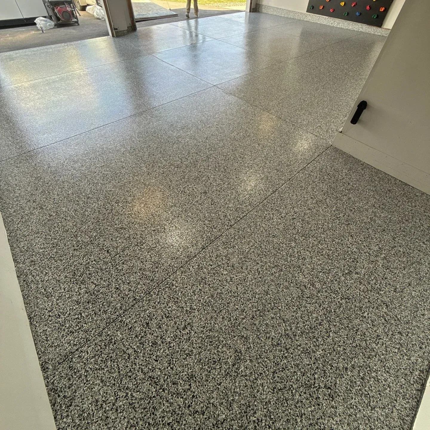 A garage with a newly-coated black, gray, and white flecked concrete floor. A small rock climbing wall is visible in the background.
