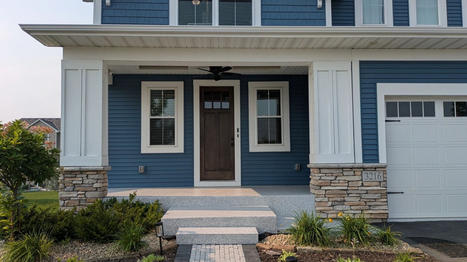 A blue house with white trim and gray flecked concrete coated patio porch and entry steps.