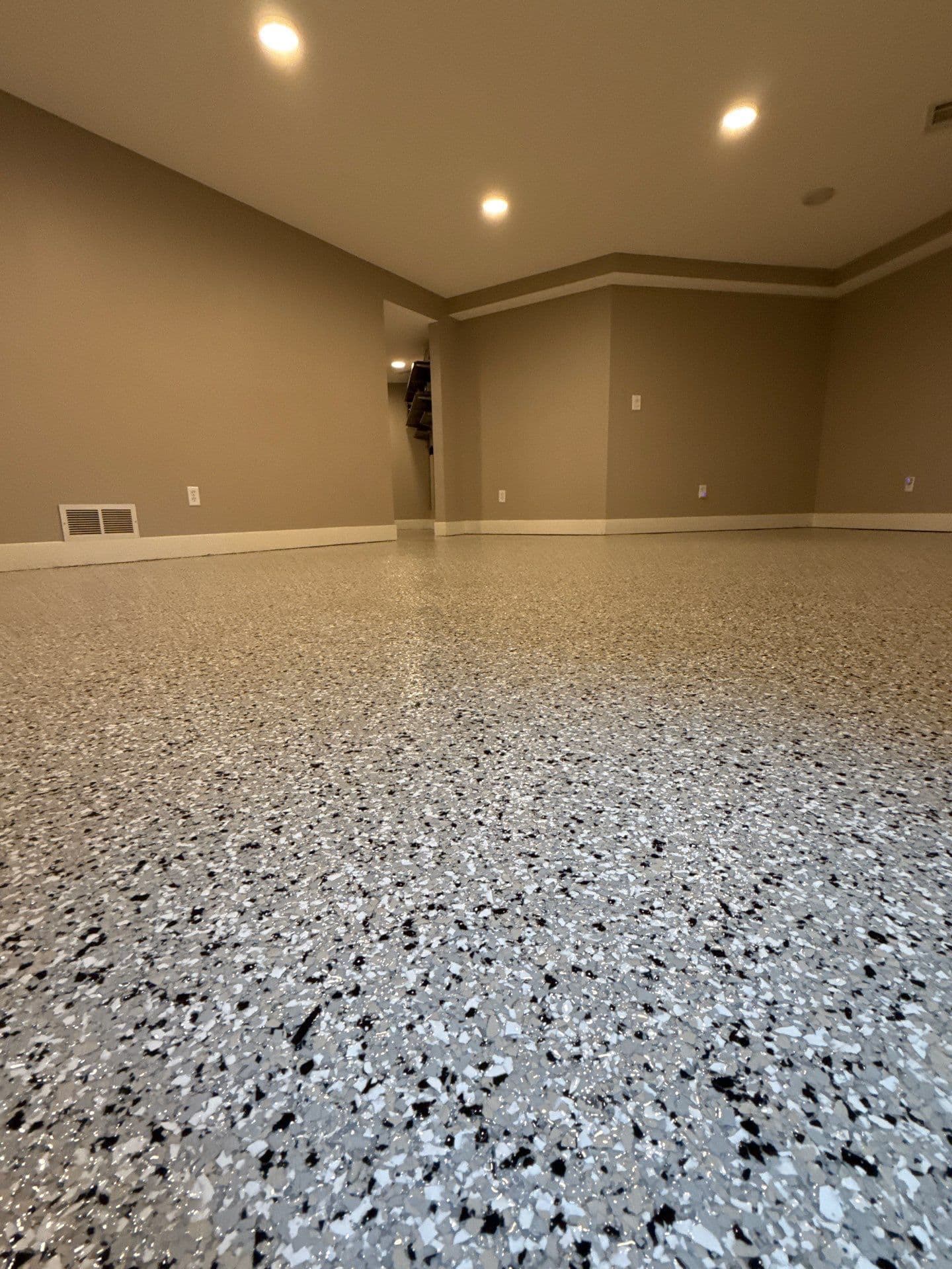 A finished basement with tan walls and light gray, white, and black flecked concrete coated flooring