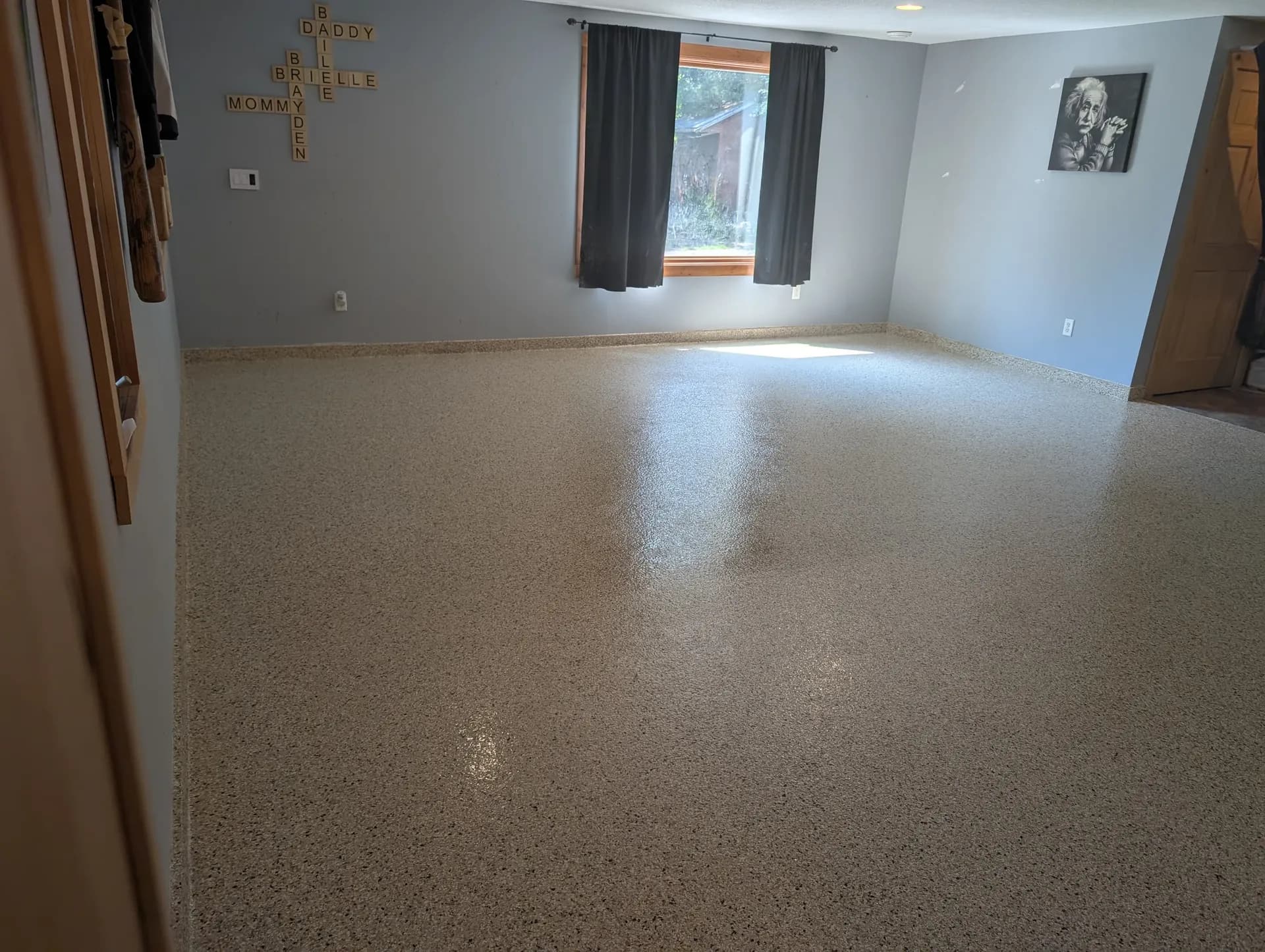 A finished basement with new light tan flecked concrete coated flooring.