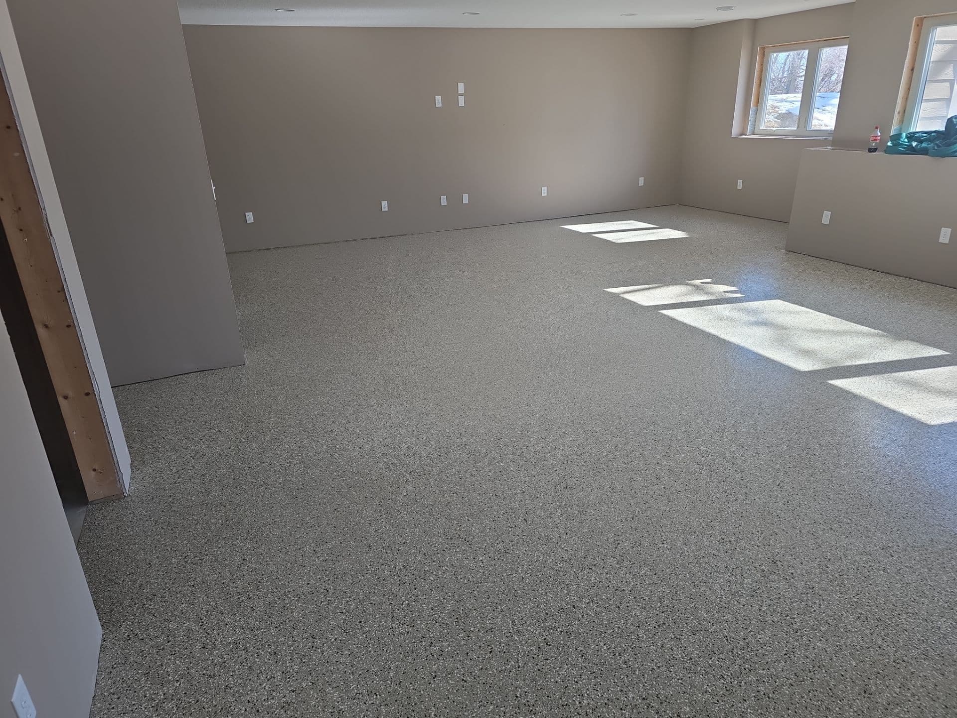 A gray, finished basement with newly-coated black, white, and gray flecked polyurea flake concrete flooring.