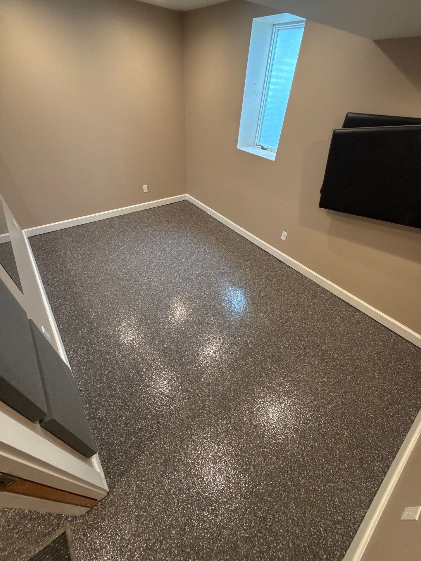 A tan, finished basement space with newly-coated gray flecked polyurea flake concrete flooring.