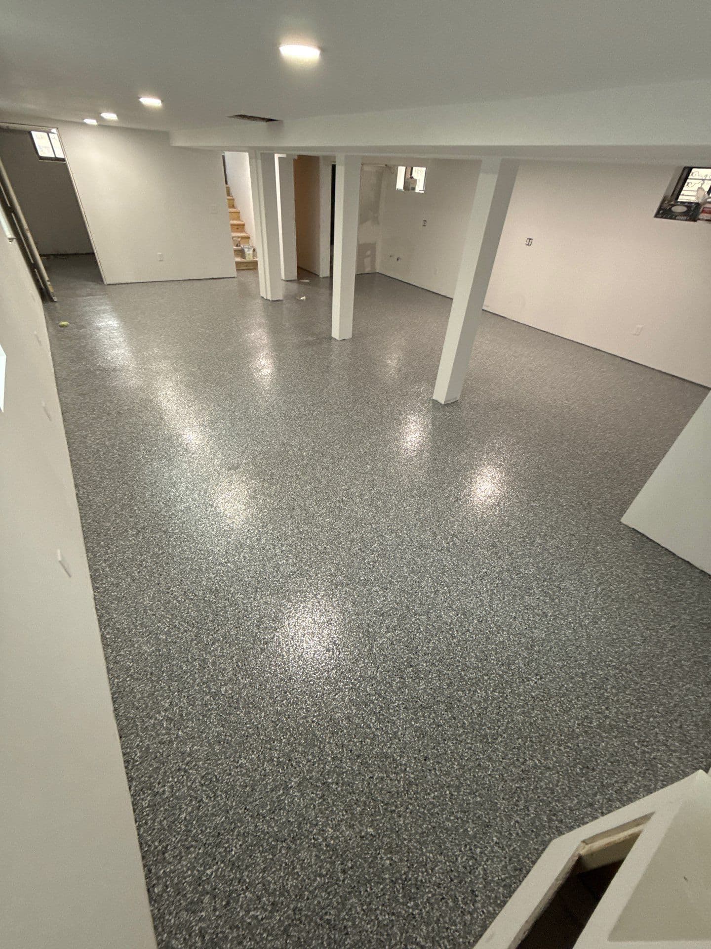 A white, finished basement with newly-coated black, white, and dark gray flecked concrete flooring.