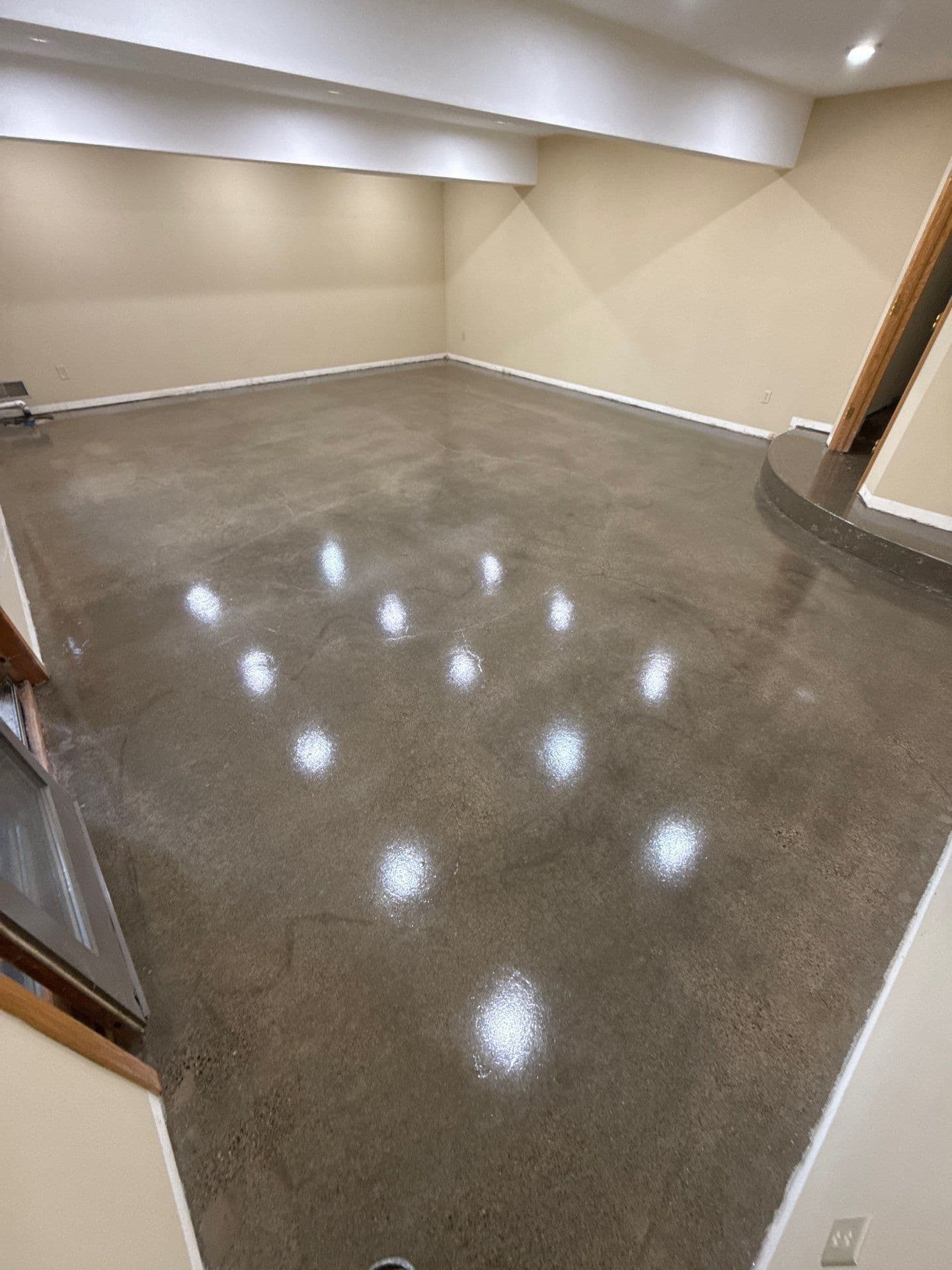 A tan, finished basement space with newly-coated dark gray Grind and Seal concrete flooring.