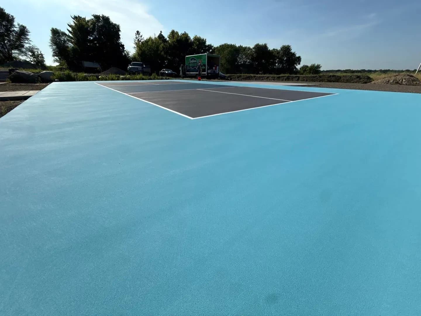 A newly-coated gray, blue, and white outdoor pickleball concrete flooring court.